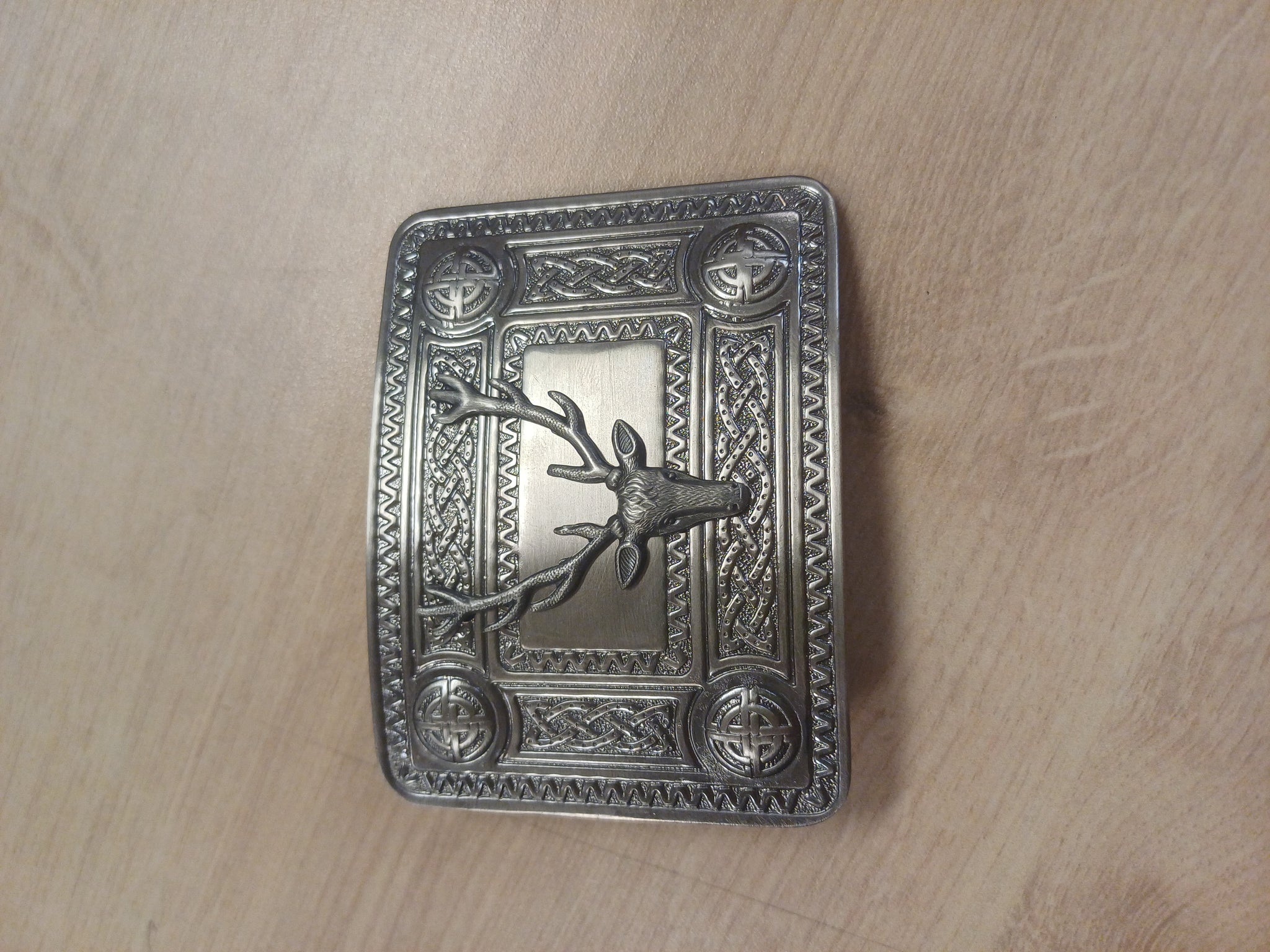 Decorative metal buckle with deer design on a wooden surface