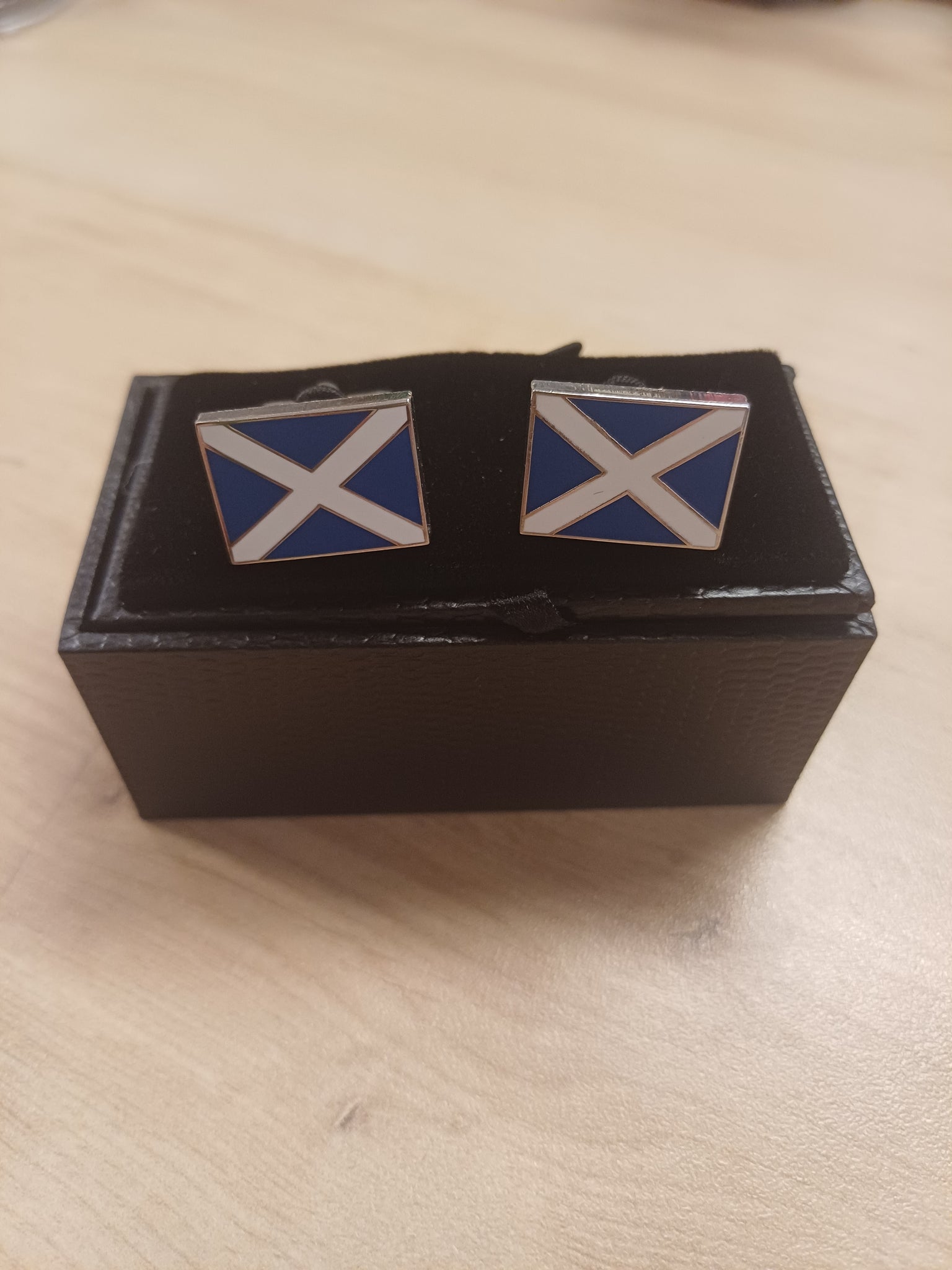 Pair of cufflinks with a blue and white design in a black box on a beige surface