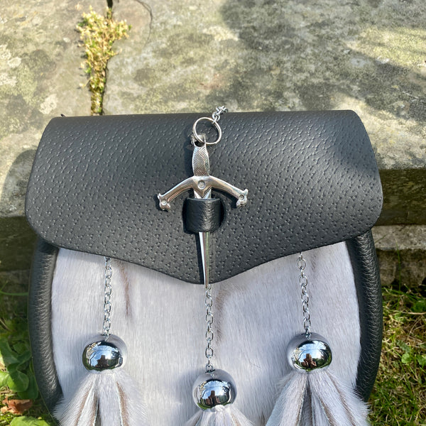 A black leather sporran with a silver dagger-shaped front clasp and light gray fur tassels