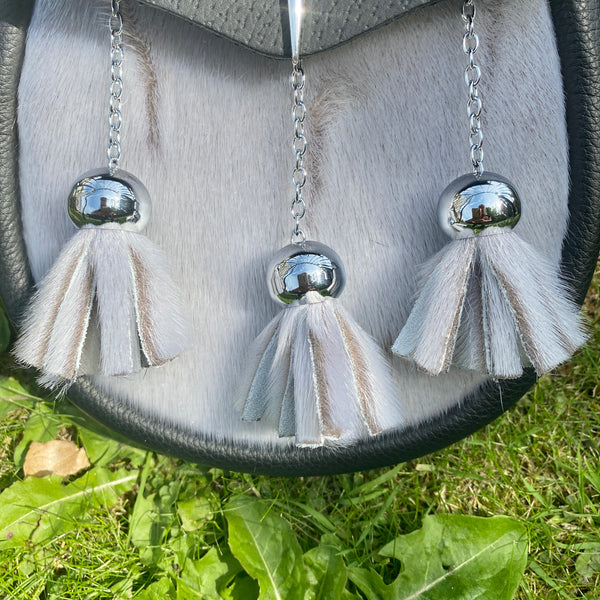 A close-up of a black leather sporran with a light gray sealskin, featuring three hanging tassels with chains.