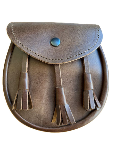 A cognac brown leather sporran with a flap closure secured by a metal snap button, featuring three leather tassels